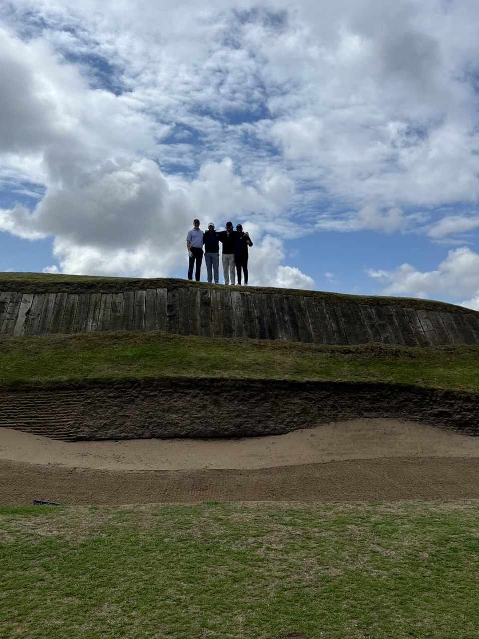 Five golfers standing atop the edge of Gumbley's Bunker, a massive sand dune with railway sleepers, at Southport & Ainsdale